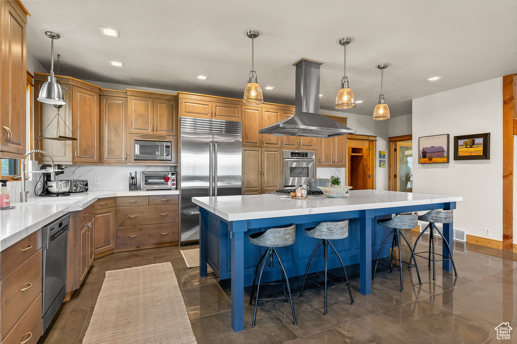 Kitchen with hanging light fixtures, built in appliances, a kitchen island, and island range hood