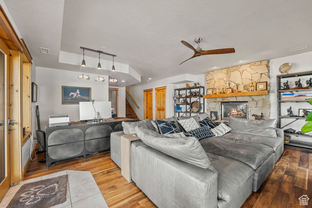 Living room featuring a stone fireplace, hardwood / wood-style flooring, ceiling fan, and a textured ceiling