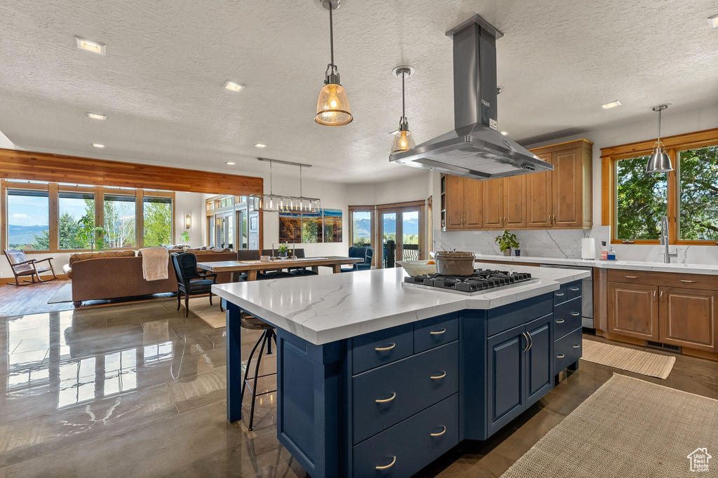 Kitchen with a wealth of natural light, island exhaust hood, a center island, and decorative light fixtures