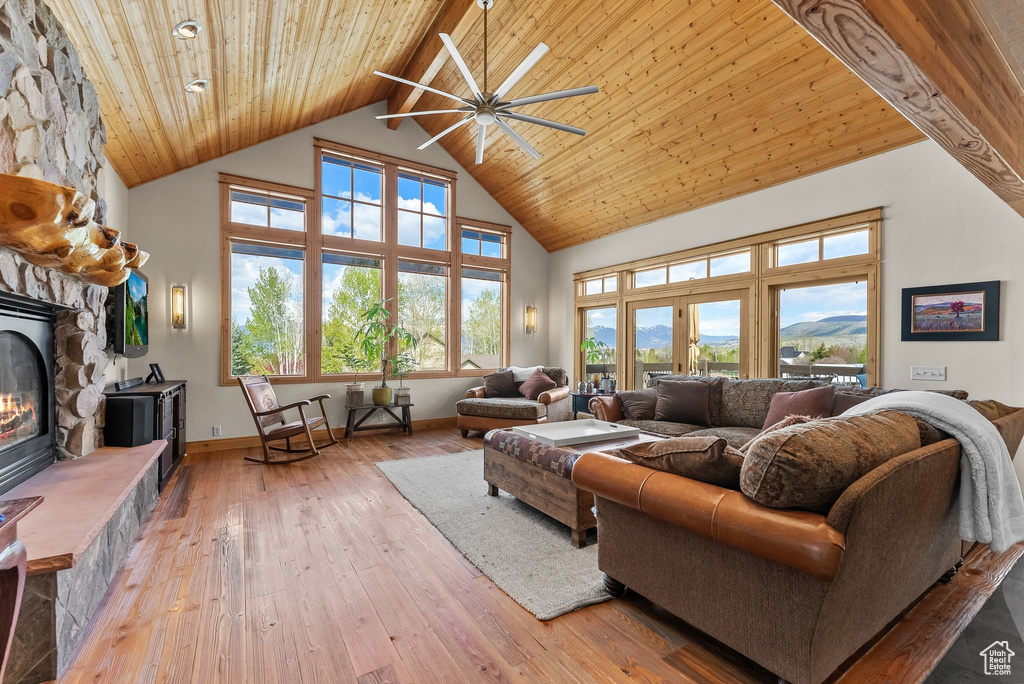 Living room with high vaulted ceiling, wood-type flooring, a stone fireplace, and plenty of natural light