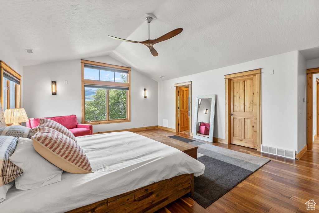 Bedroom with hardwood / wood-style flooring, lofted ceiling, ceiling fan, and a textured ceiling