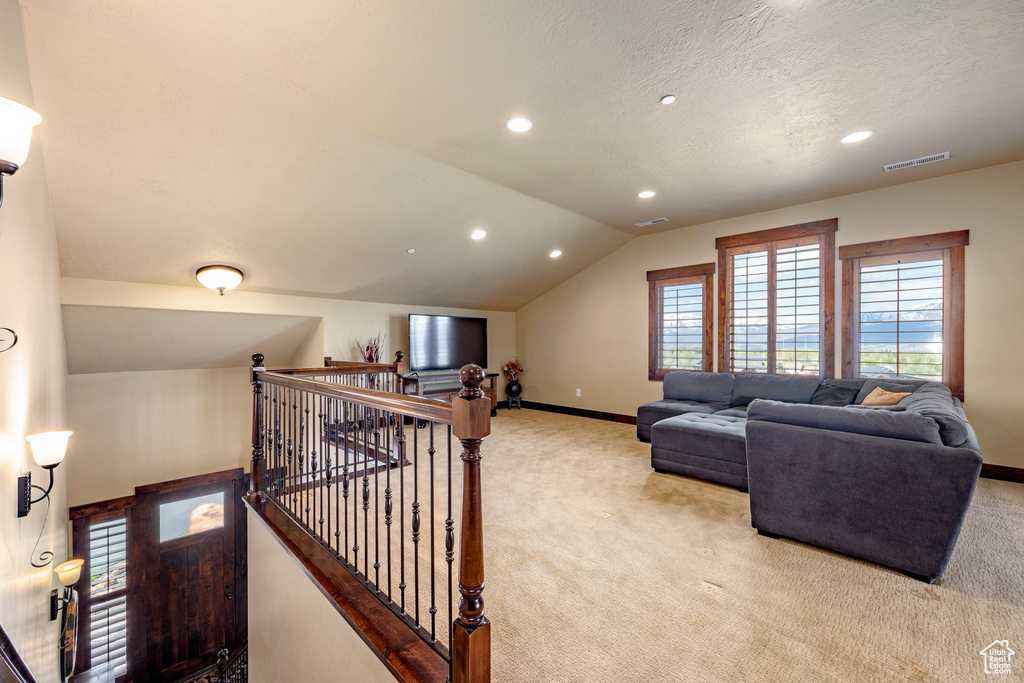 Living room with light carpet, a healthy amount of sunlight, a textured ceiling, and vaulted ceiling