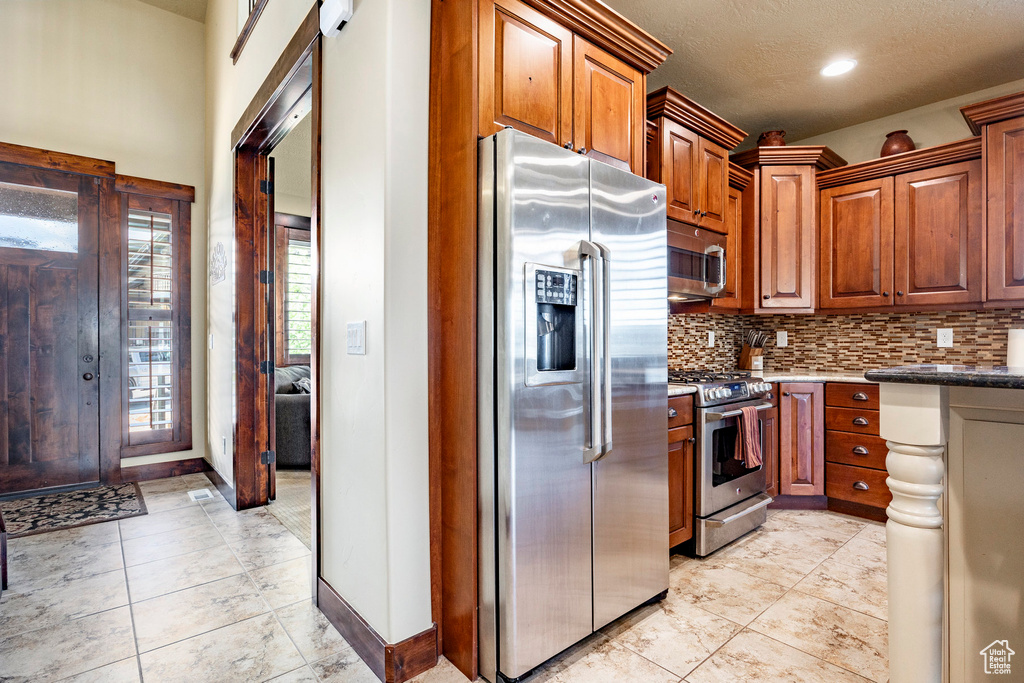 Kitchen featuring stainless steel appliances, light tile floors, dark stone countertops, and backsplash