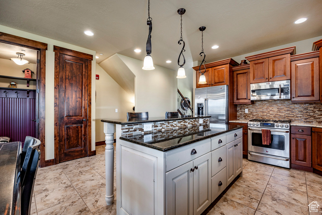 Kitchen featuring dark stone counters, a kitchen island, backsplash, hanging light fixtures, and appliances with stainless steel finishes