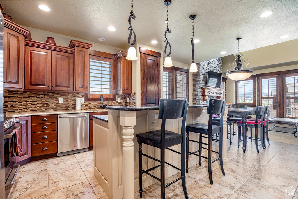 Kitchen featuring stainless steel appliances, light tile flooring, pendant lighting, backsplash, and a center island