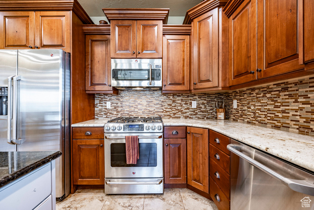 Kitchen with light stone counters, appliances with stainless steel finishes, tasteful backsplash, and light tile floors