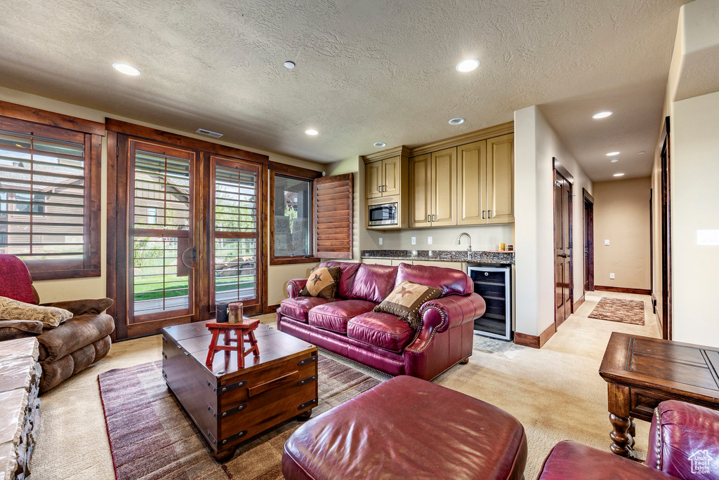 Carpeted living room with wine cooler, sink, and a textured ceiling