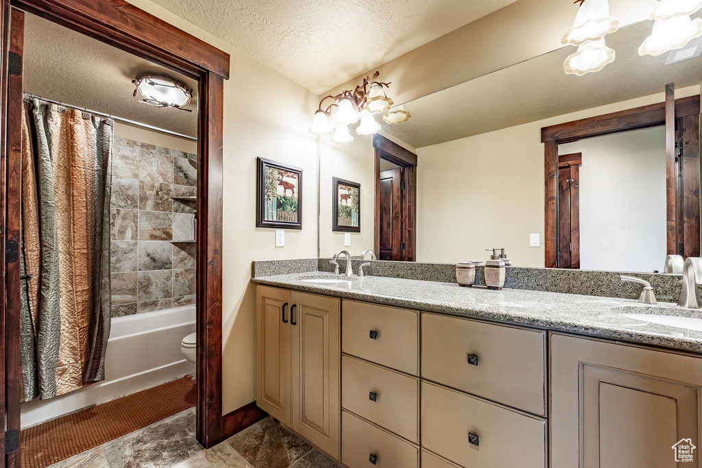 Full bathroom featuring a textured ceiling, double sink vanity, tile floors, shower / tub combo with curtain, and toilet