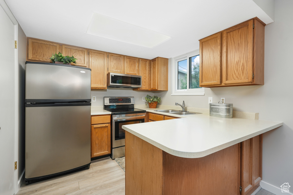 Kitchen featuring stainless steel appliances, light hardwood / wood-style floors, kitchen peninsula, and sink