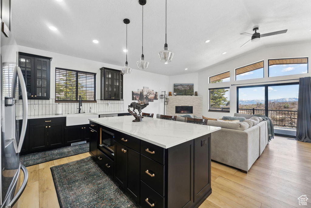 Kitchen with a center island, light hardwood / wood-style floors, a fireplace, appliances with stainless steel finishes, and tasteful backsplash