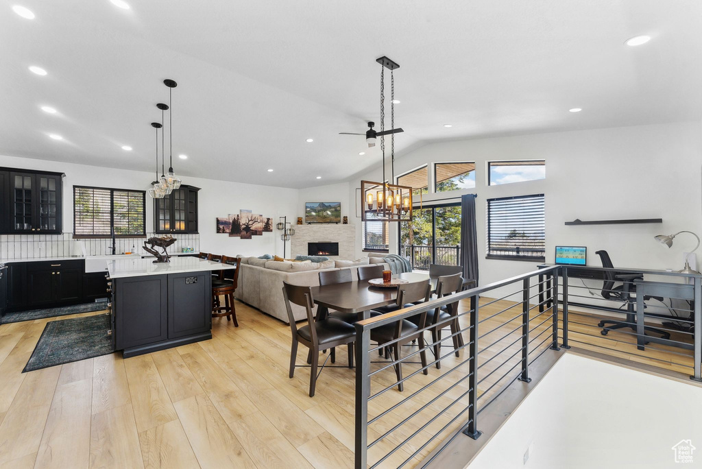 Dining space featuring ceiling fan with notable chandelier, light hardwood / wood-style floors, and vaulted ceiling