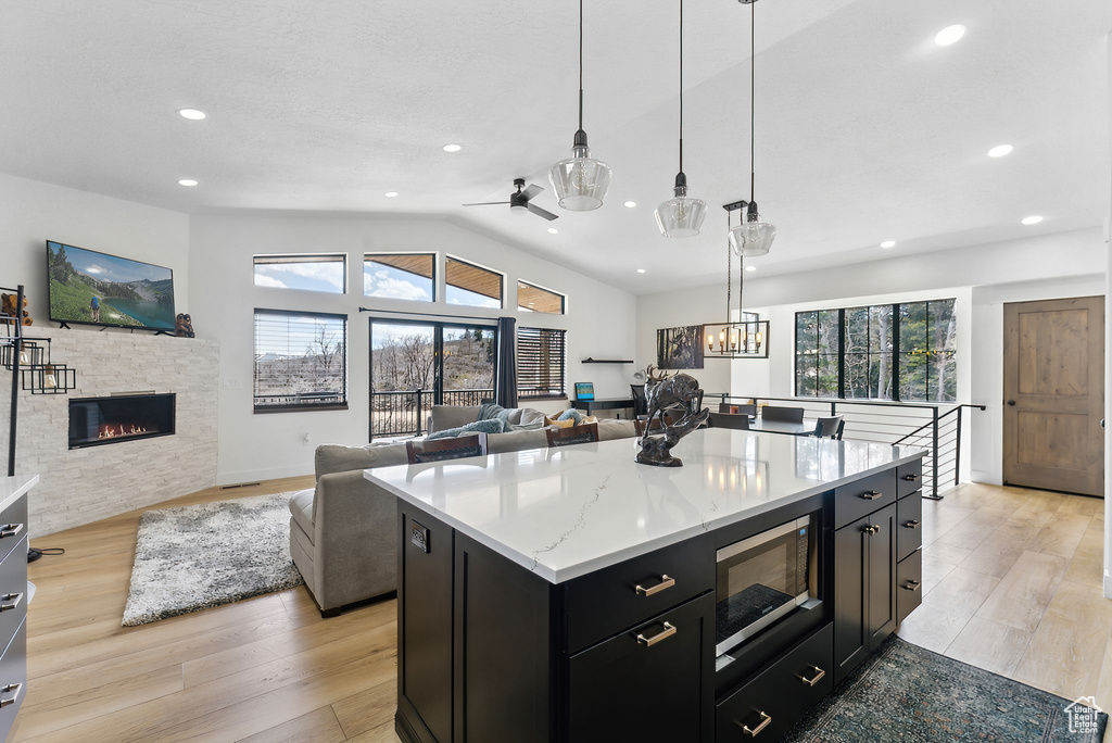 Kitchen with light stone counters, a kitchen island, built in microwave, decorative light fixtures, and vaulted ceiling