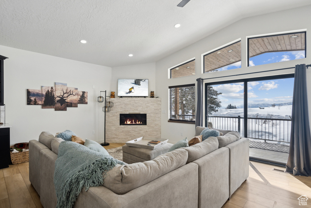Living room with lofted ceiling, a stone fireplace, light hardwood / wood-style flooring, and a textured ceiling