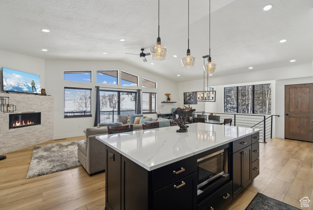 Kitchen with a center island, black microwave, a textured ceiling, pendant lighting, and light stone countertops