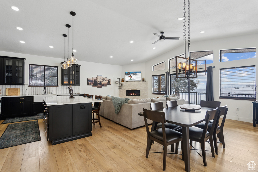 Dining area with lofted ceiling, a stone fireplace, ceiling fan, and light wood-type flooring
