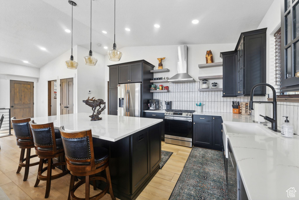 Kitchen with tasteful backsplash, stainless steel appliances, a kitchen island, wall chimney range hood, and lofted ceiling