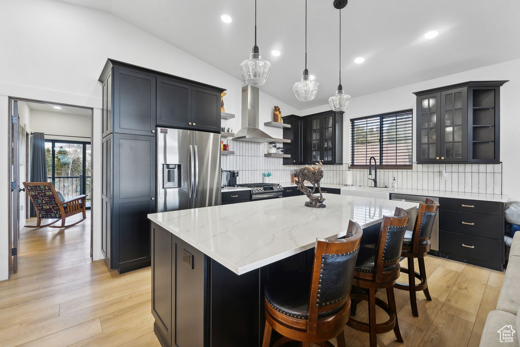Kitchen featuring light hardwood / wood-style flooring, tasteful backsplash, wall chimney range hood, a center island, and appliances with stainless steel finishes