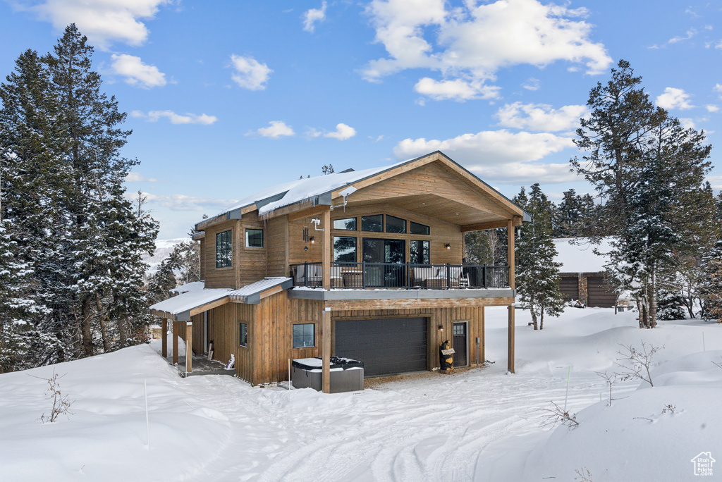 Snow covered back of property featuring a garage and a balcony