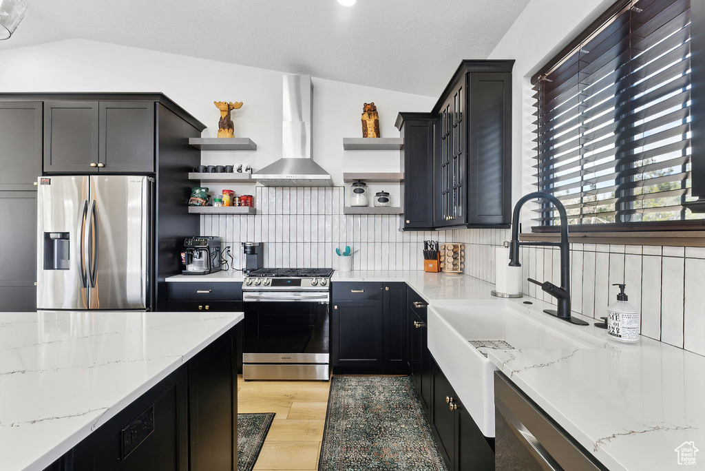 Kitchen with light hardwood / wood-style flooring, stainless steel appliances, vaulted ceiling, range hood, and backsplash