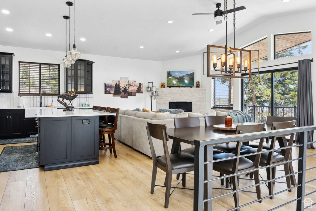 Dining area featuring a fireplace, light wood-type flooring, vaulted ceiling, and ceiling fan with notable chandelier