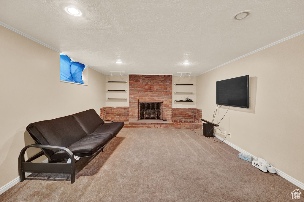 Carpeted living room featuring a textured ceiling, a fireplace, crown molding, and brick wall