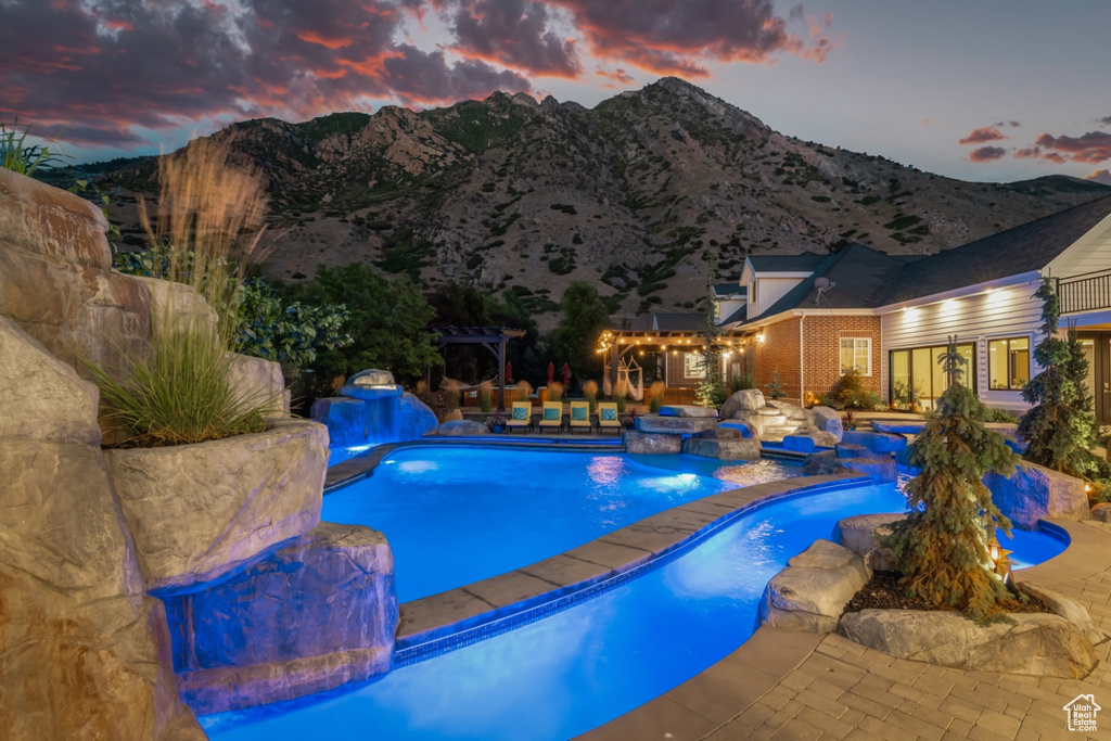 Pool at dusk featuring a patio area, pool water feature, and a mountain view