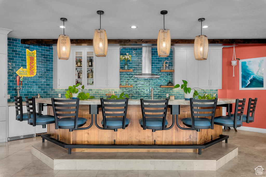 Bar with wall chimney range hood, white cabinetry, pendant lighting, and light tile floors