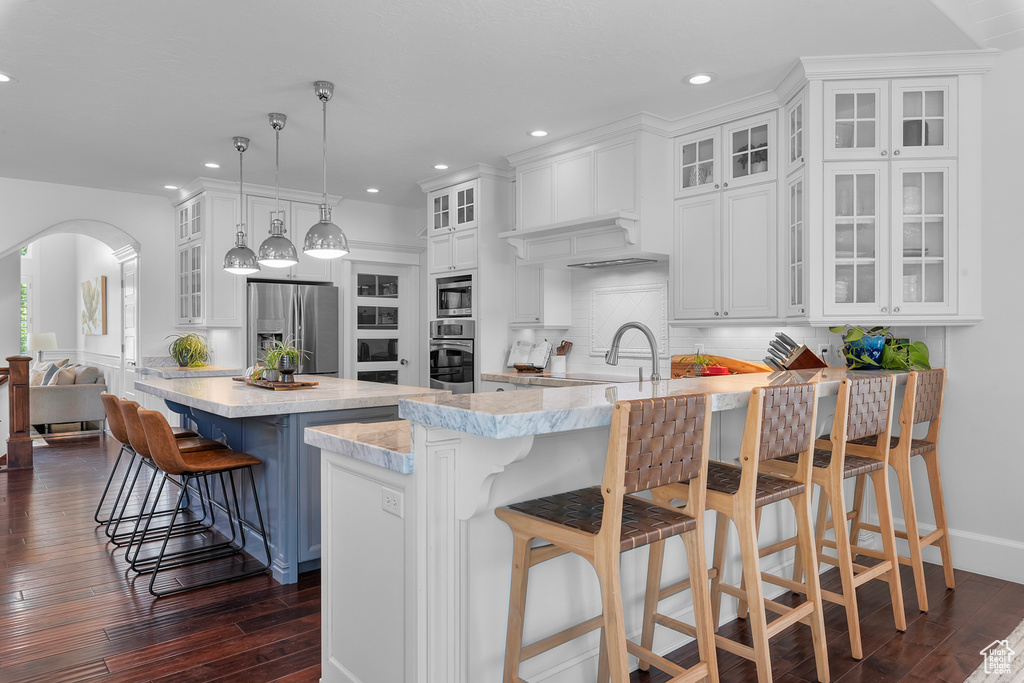 Kitchen featuring dark wood-type flooring, stainless steel appliances, decorative light fixtures, a breakfast bar, and tasteful backsplash