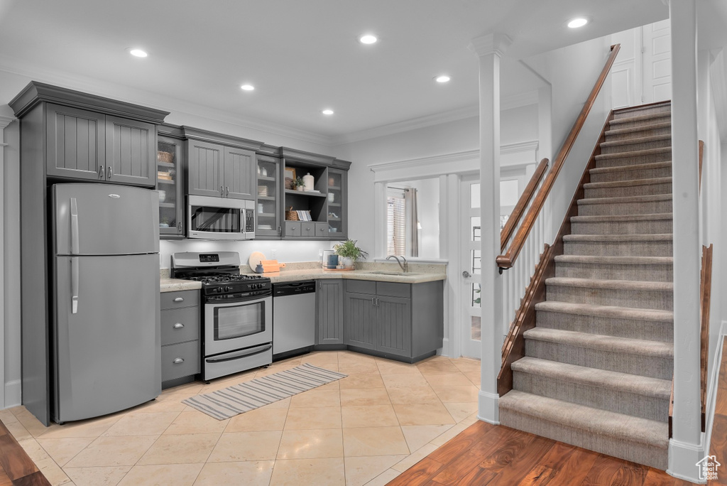 Kitchen featuring light hardwood / wood-style floors, ornamental molding, gray cabinets, appliances with stainless steel finishes, and decorative columns