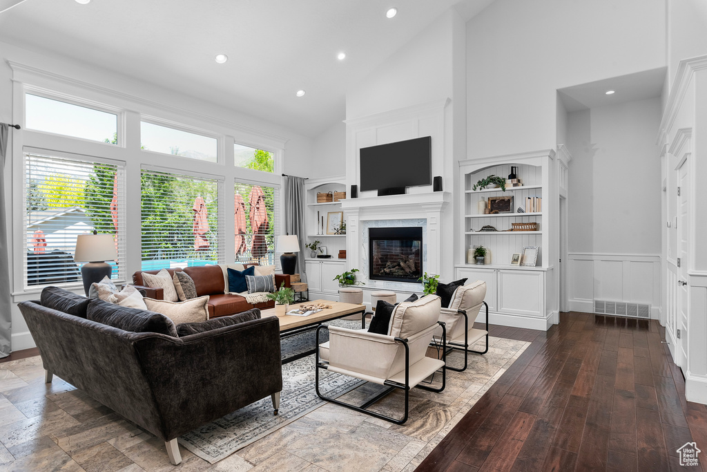 Living room with high vaulted ceiling, built in shelves, a fireplace, and wood-type flooring