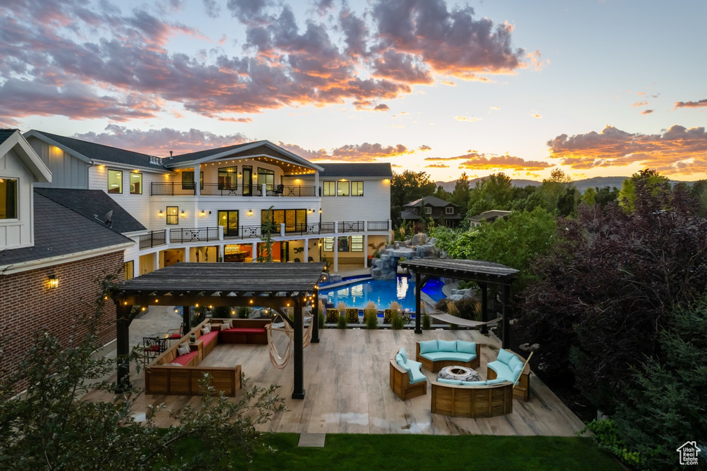 Back house at dusk with a patio, a pool side deck, an outdoor living space with a fire pit, and a balcony