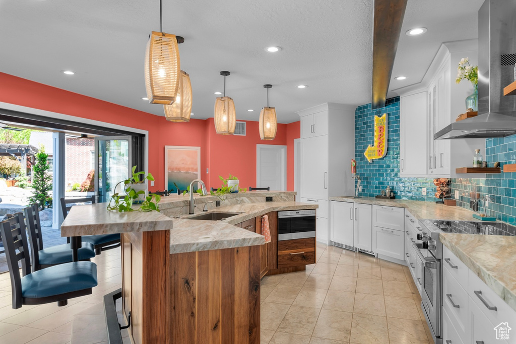 Kitchen with sink, white cabinets, pendant lighting, and wall chimney exhaust hood