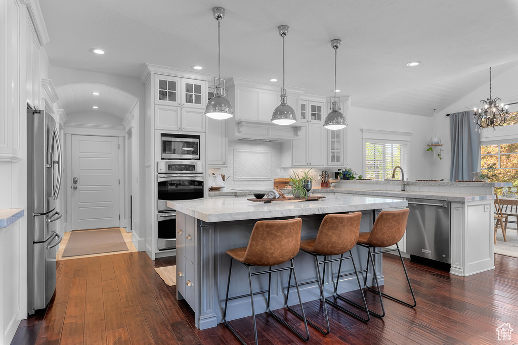 Kitchen featuring dark hardwood / wood-style flooring, lofted ceiling, a center island, white cabinets, and appliances with stainless steel finishes