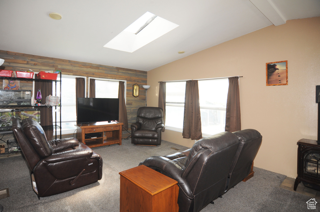 Living room with carpet, wooden walls, and vaulted ceiling with skylight