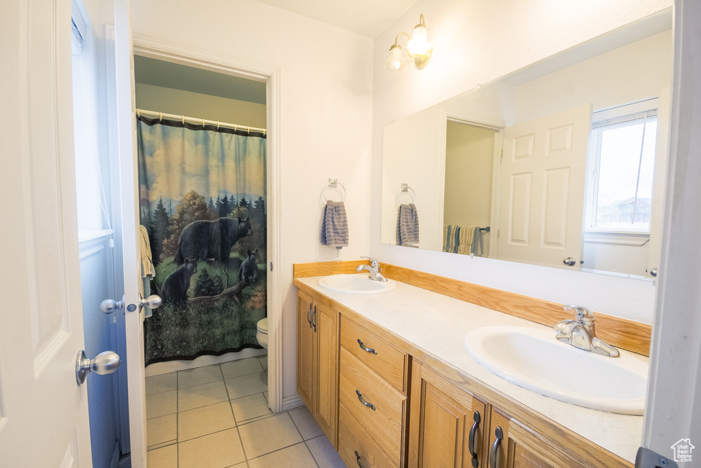 Bathroom with tile flooring, oversized vanity, double sink, and toilet