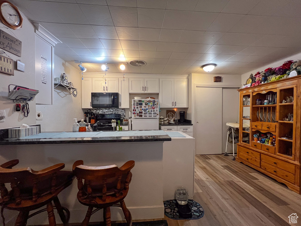 Kitchen featuring white fridge, light hardwood / wood-style flooring, kitchen peninsula, white cabinets, and electric stove