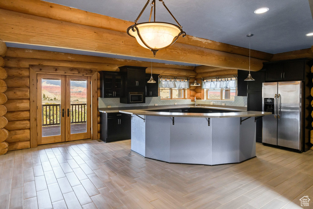Kitchen with hanging light fixtures, stainless steel appliances, dark cabinets, and a center island