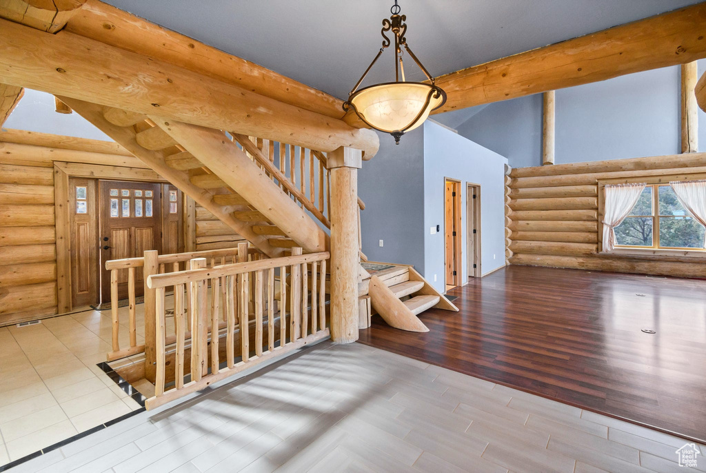Unfurnished living room with stairway, log walls, beamed ceiling, and wood finished floors