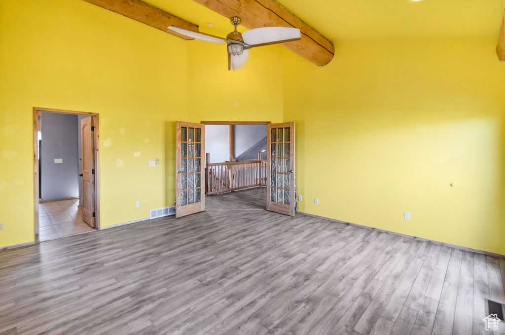 Empty room featuring beamed ceiling, light wood-type flooring, and visible vents