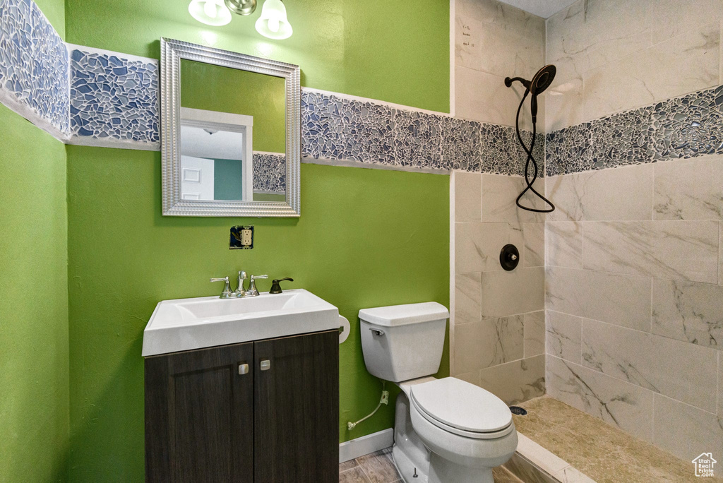 Full bathroom featuring toilet, baseboards, tiled shower, and vanity