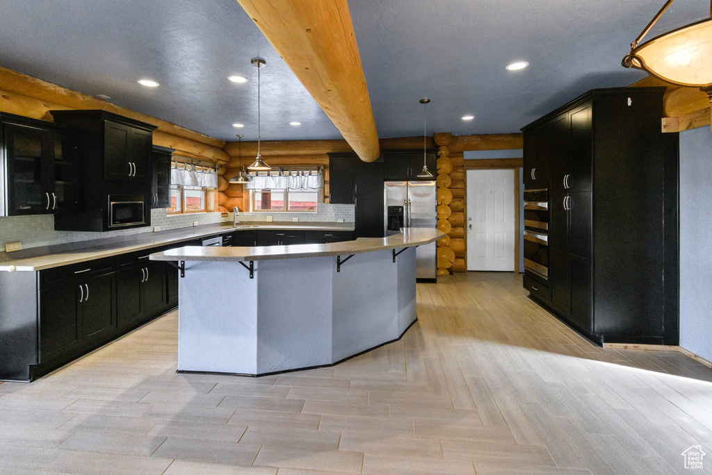 Kitchen with dark cabinets, a breakfast bar, a kitchen island, backsplash, and decorative light fixtures