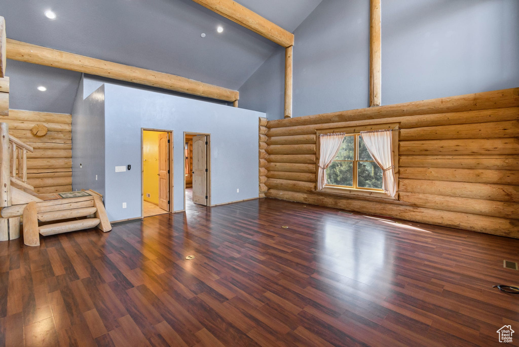 Unfurnished living room with high vaulted ceiling, beam ceiling, log walls, and dark wood-style floors