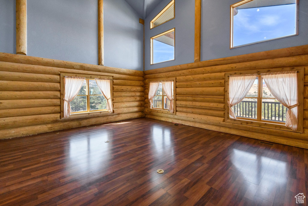 Spare room featuring dark wood-style floors, a high ceiling, visible vents, and log walls