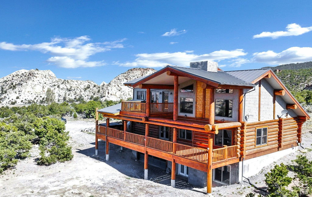 Snow covered property featuring a deck with mountain view, a standing seam roof, metal roof, a balcony, and log siding