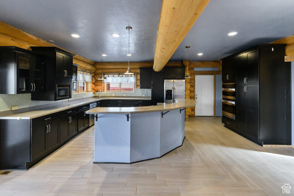 Kitchen featuring dark cabinets, a breakfast bar, light countertops, appliances with stainless steel finishes, and a center island