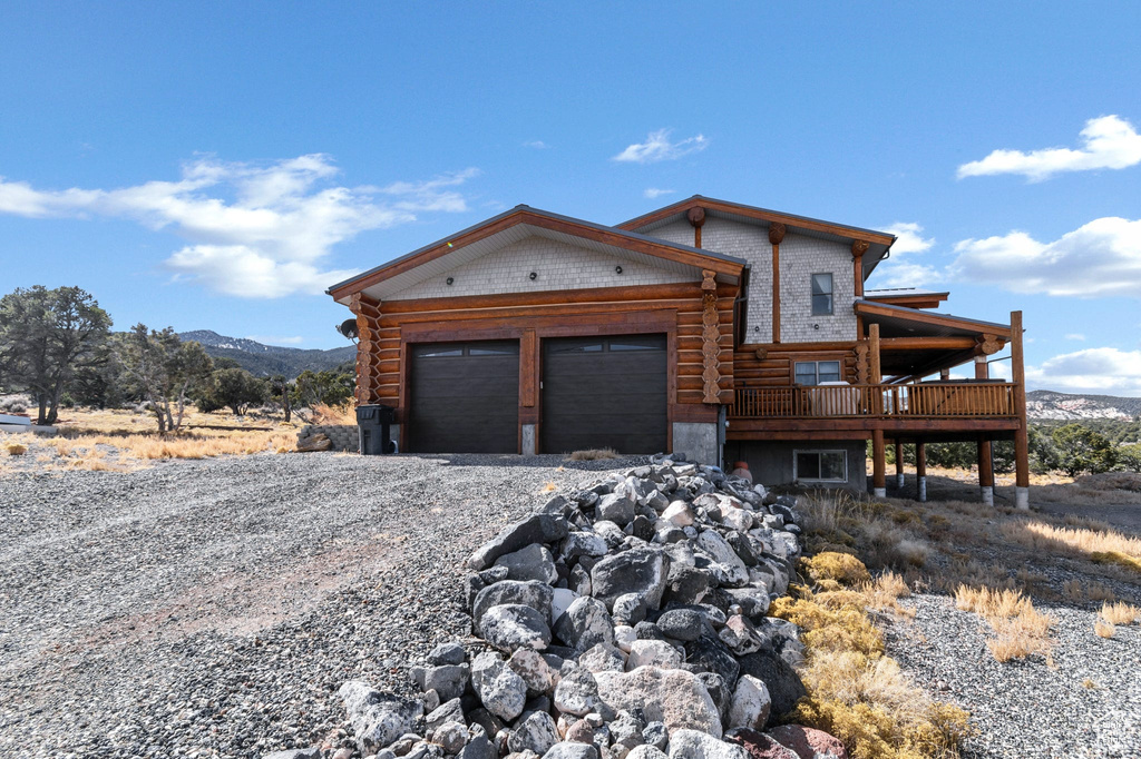 Log cabin with a garage, log exterior, a deck with mountain view, and driveway
