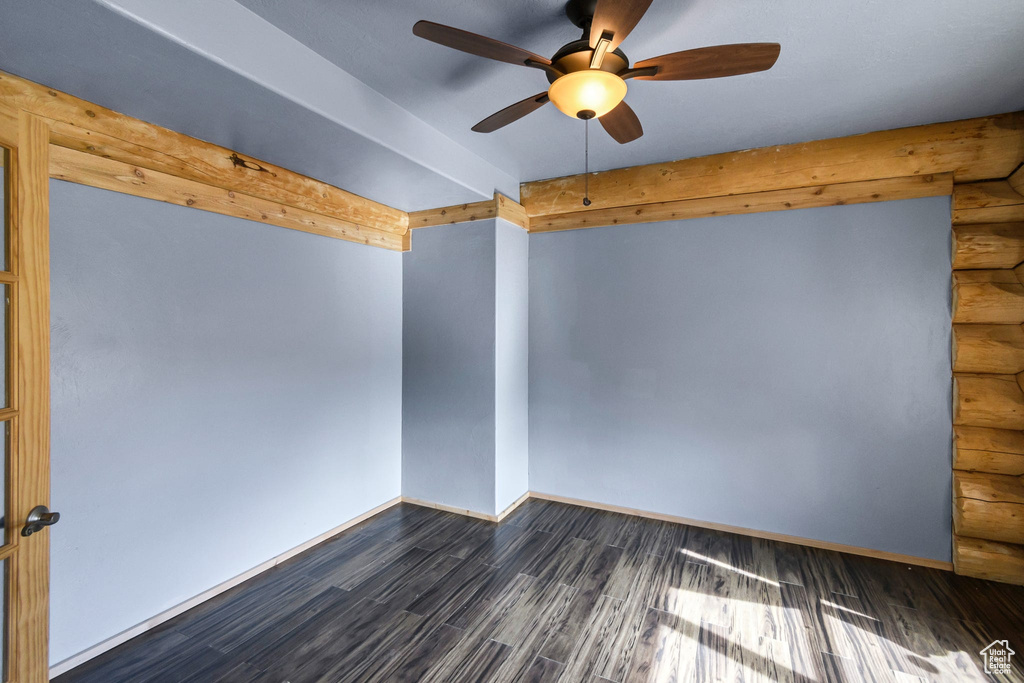 Spare room with dark wood-style flooring, rustic walls, baseboards, and beam ceiling