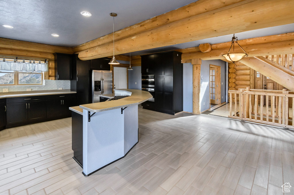 Kitchen with stainless steel appliances, light countertops, hanging light fixtures, an island with sink, and a kitchen bar