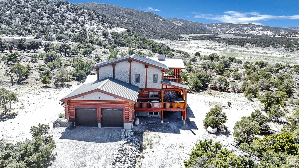 View of front of home with a garage, a deck with mountain view, gravel driveway, and log siding