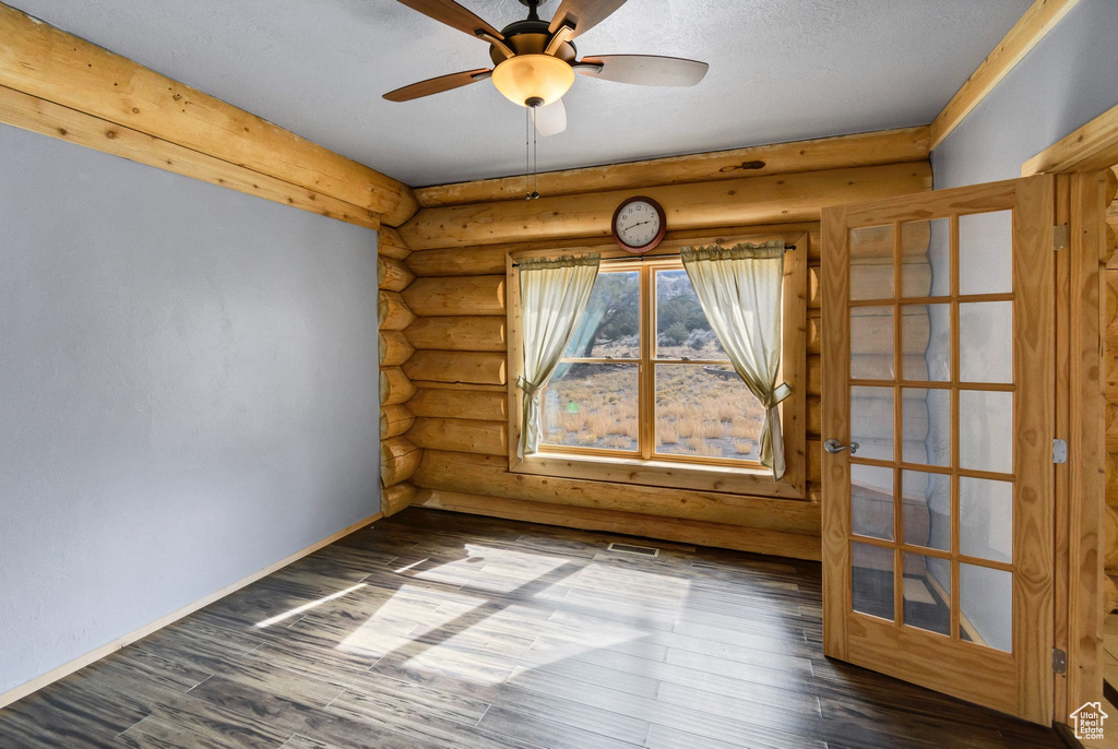 Spare room with ceiling fan, dark wood-style flooring, visible vents, baseboards, and log walls